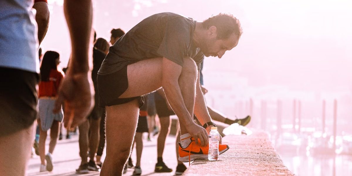 Man ties his shoes before a run outdoors with a bottle of water nearby.